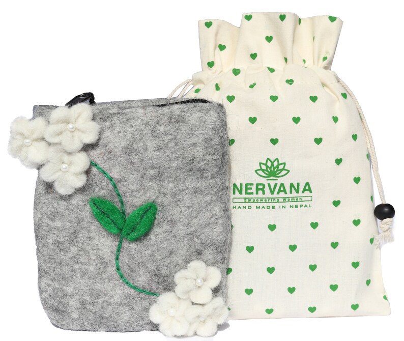 Puede incluir: Una bolsa de fieltro gris con flores de fieltro blanco y hojas de fieltro verde. La bolsa est&aacute; en una bolsa de algod&oacute;n blanco con cord&oacute;n con corazones verdes y el texto "NERVANA Empowering Women HAND MADE IN NEPAL".