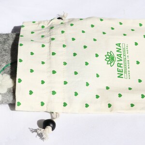Puede incluir: Una bolsa de fieltro gris con un adorno de flor de fieltro blanco y un tallo verde. La bolsa est&aacute; en una bolsa de cord&oacute;n blanco con un patr&oacute;n de corazones verdes y el texto "NERVANA FELTED TREASURES HAND MADE IN NEPAL".