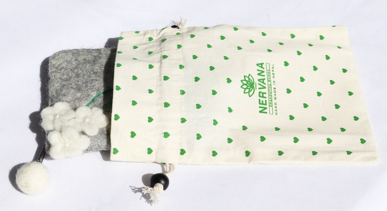 Puede incluir: Una bolsa de fieltro gris con un adorno de flor de fieltro blanco y un tallo verde. La bolsa est&aacute; en una bolsa de cord&oacute;n blanco con un patr&oacute;n de corazones verdes y el texto "NERVANA FELTED TREASURES HAND MADE IN NEPAL".