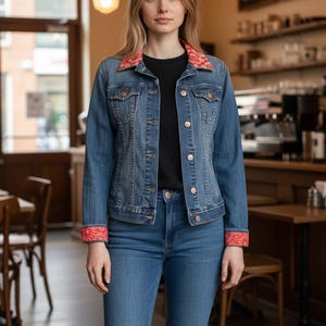 May include: A blue denim jacket featuring a red and white floral patterned collar and matching cuffs, worn over a black shirt and blue denim jeans. The jacket includes metal buttons down the front and two chest pockets with buttoned flaps.