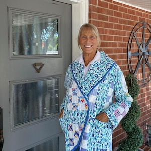 May include: A quilted jacket in shades of blue, white, and green. The jacket features a patchwork design with various patterns and a contrasting blue trim. It has pockets and is worn over a white collared shirt.