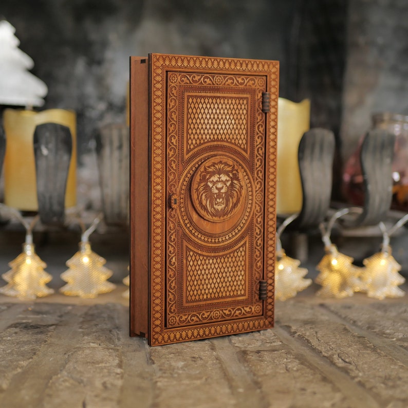 Pu&ograve; includere: Una scatola di legno con un design a testa di leone intagliato sul davanti. La scatola ha una porta incernierata e dettagli intricati.