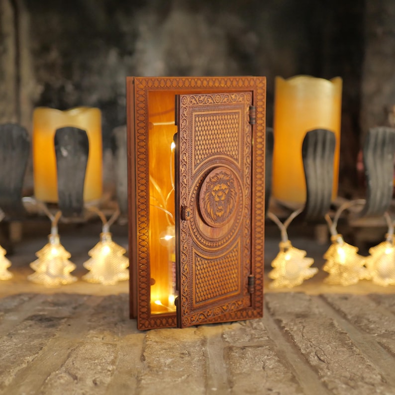 Pu&ograve; includere: Una scatola di legno con un design a testa di leone sulla porta. La porta &egrave; aperta e ci sono luci all'interno della scatola.