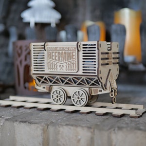 May include: A wooden model train car with the words "Beer Mining Ink. Beermine" on the side. The car is on a wooden track and has wheels.