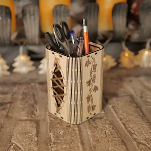 May include: A wooden pencil holder with a vine design and a rope detail. The holder is filled with pens, pencils, and scissors.