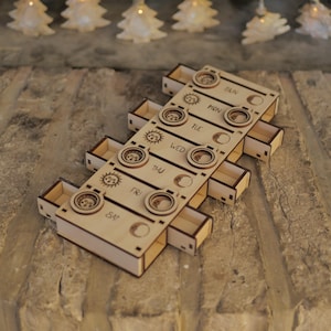 May include: Wooden box with seven drawers, each labeled with a day of the week. Each drawer has a sun and moon design.