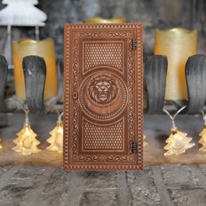 May include: A wooden box with a lion head design carved into the front. The box has a hinged lid and ornate details around the edges.