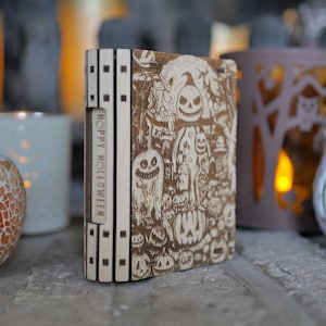 Könnte beinhalten: Eine Holzkiste mit Halloween-Motiv. Die Kiste ist mit verschiedenen gruseligen Figuren und Symbolen verziert, darunter Kürbisse, Geister und Fledermäuse. Der Text "Happy Halloween" ist auf der Seite der Kiste eingraviert.