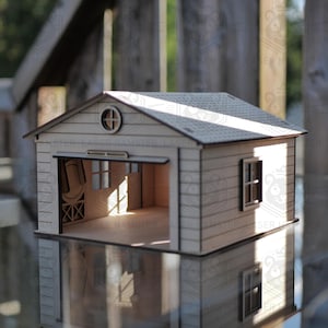 Puede incluir: Un modelo de garaje de madera en miniatura con un exterior de color claro y un techo detallado. La puerta del garaje está abierta, revelando el interior. Una pequeña ventana redonda está encima de la puerta del garaje. El modelo se refleja en la superficie de abajo.