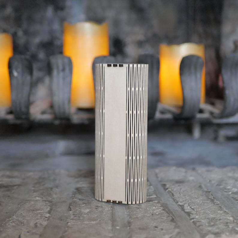 Op de afbeelding: Een houten kaarsenhouder met een geometrisch patroon. De houder is lichtbruin en heeft een natuurlijke houten afwerking. Hij staat op een bakstenen oppervlak voor een open haard.