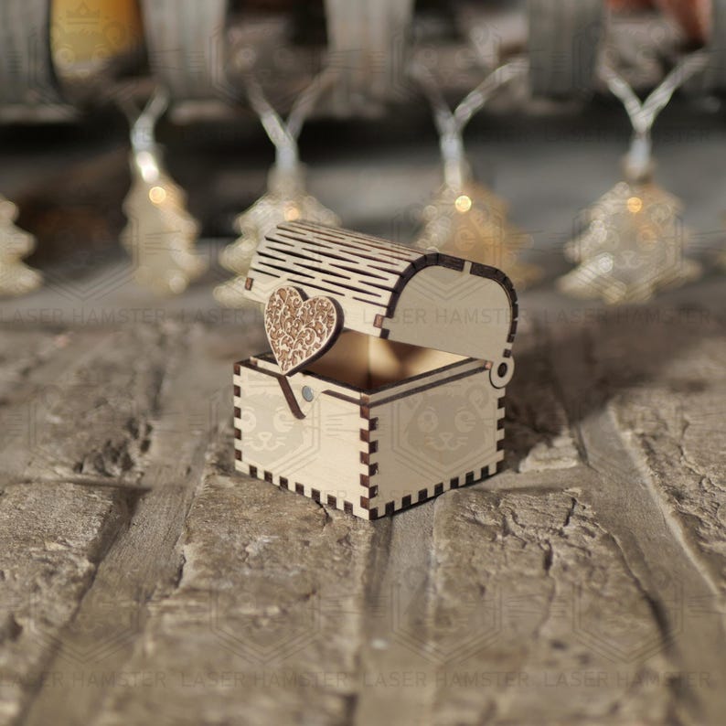 May include: A small, open wooden treasure chest with a heart-shaped accent. The chest is made of light-colored wood and has a decorative heart on the lid. The chest is sitting on a brick surface.