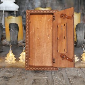 Pu&ograve; includere: Una scatola di legno con un coperchio incernierato che si apre per rivelare uno spazio vuoto all'interno. La scatola ha un bordo decorativo ed &egrave; realizzata in legno marrone chiaro.