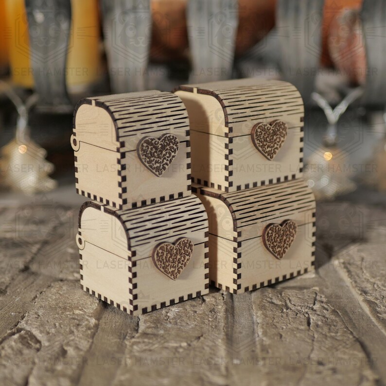 May include: Four small, wooden treasure chests with arched lids and heart-shaped embellishments. The chests are light brown with decorative etched lines and a laser-cut heart on the front. They are stacked on a textured surface.
