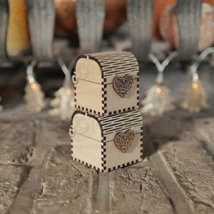 May include: Two small, wooden treasure chests stacked on top of each other. Each chest has a heart-shaped embellishment and a hinged lid. The chests are made of light-colored wood with dark accents.
