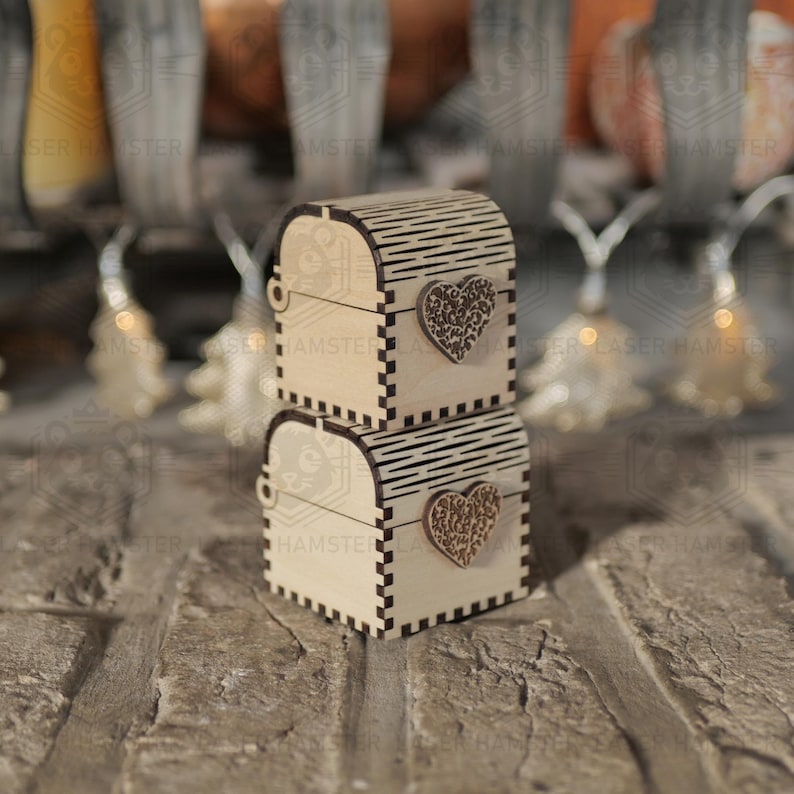 May include: Two small, wooden treasure chests stacked on top of each other. Each chest has a heart-shaped embellishment and a hinged lid. The chests are made of light-colored wood with dark accents.