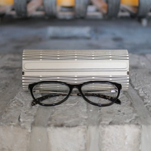 Puede incluir: Gafas con montura negra y estuche de gafas a rayas blancas y negras.