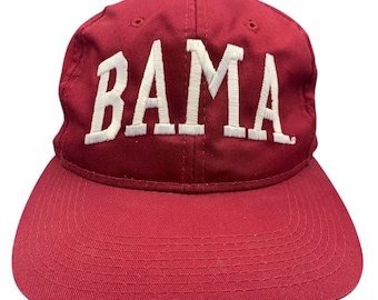 May include: A deep red baseball cap featuring the word BAMA embroidered in bold white capital letters across the front panel. The hat has a structured crown, a curved brim with tonal stitching, and small ventilation eyelets on the top panels.