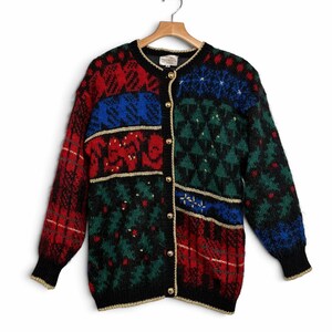 May include: A long-sleeve knit cardigan sweater featuring a multi-colored patchwork pattern in red, blue, green, and black. The garment includes gold-toned buttons down the front, a round neckline, and gold-colored trim along the edges and cuffs.