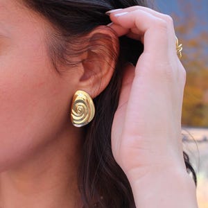 Puede incluir: Pendientes de oro con diseño de espiral. Los pendientes son de forma ovalada y tienen una superficie texturizada.