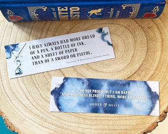 May include: Two blue and white watercolor bookmarks with inspirational quotes. The first bookmark features a quote from "The Count of Monte Cristo" by Alexandre Dumas. The second bookmark features a quote about happiness and pride.