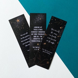May include: Three black bookmarks with gold foil accents and star designs. The bookmarks feature quotes about stars and the night sky. The quotes are: "We are all in the gutter, but some of us are looking at the stars." "Looking at these stars suddenly dwarfed my own troubles and all the gravities of terrestrial life." "I have loved the stars too fondly to be fearful of the night."