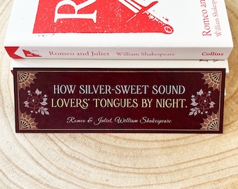 May include: A bookmark with a burgundy background and gold accents features a quote from Romeo and Juliet: "How silver-sweet sound lovers' tongues by night."