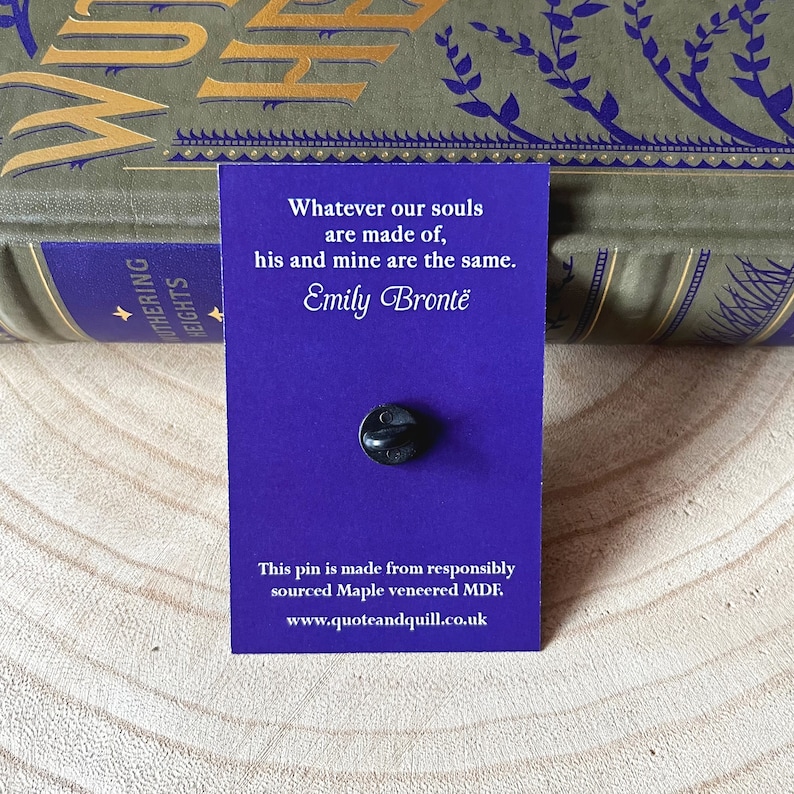 Puede incluir: Tarjeta morada con una cita de Emily Bront&euml; de "Cumbres Borrascosas": "Cualquiera que sea la naturaleza de nuestras almas, la suya y la m&iacute;a son las mismas." La tarjeta tiene un alfiler negro y un texto en la parte inferior que dice "Este pin est&aacute; hecho de MDF chapado en arce de origen responsable. www.quoteandquill.co.uk"