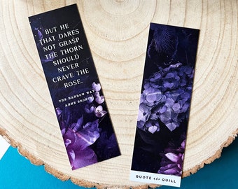 May include: Two purple floral bookmarks with quotes from "The Narrow Way" by Anne Bronte. The bookmark on the left has the quote "But he that dares not grasp the thorn should never crave the rose." The bookmark on the right has the quote "Quote and Quill".