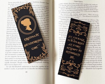 May include: Two black bookmarks with gold accents. The first bookmark features a silhouette of a woman's head with the text "Obstinate Headstrong Girl". The second bookmark features a floral design with the text "My courage always rises at every attempt to intimidate me."