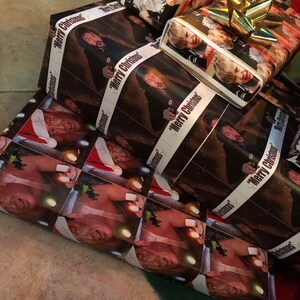 Op de afbeelding: Een stapel kerstcadeaupapier met verschillende afbeeldingen van mensen, waaronder een man met een kerstmanmuts, een man met een pistool en een jonge jongen. Het cadeaupapier heeft de tekst "Merry Christmas" erop gedrukt.