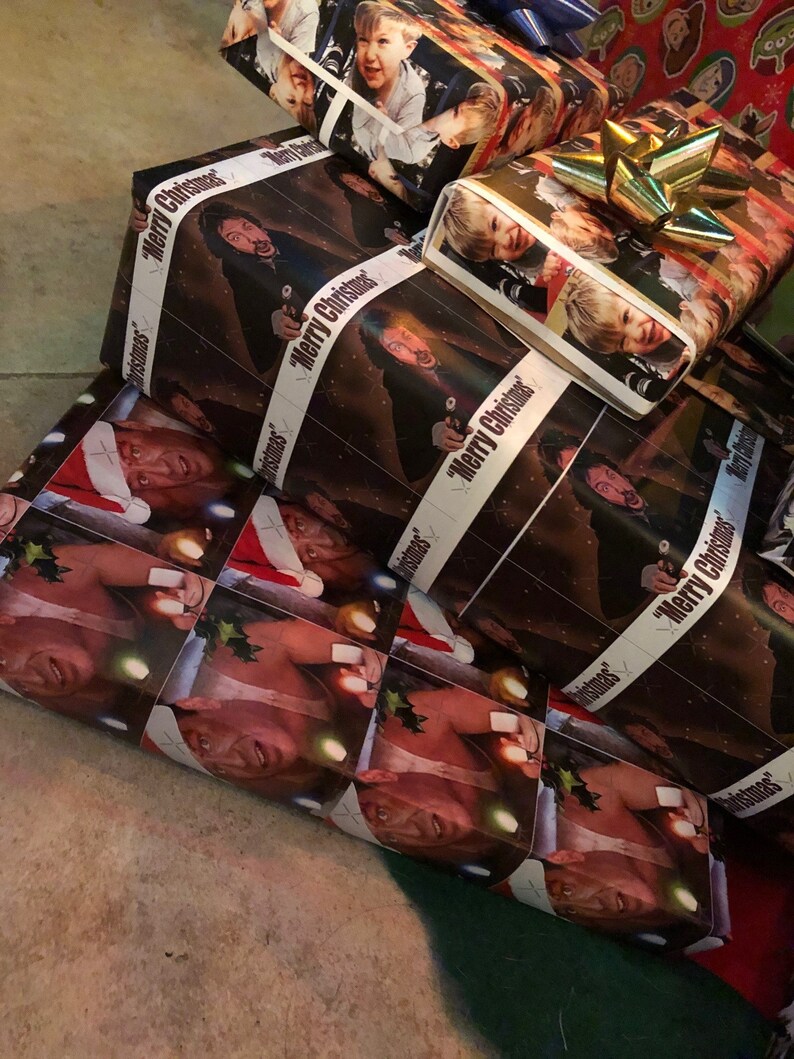 Op de afbeelding: Een stapel kerstcadeaupapier met verschillende afbeeldingen van mensen, waaronder een man met een kerstmanmuts, een man met een pistool en een jonge jongen. Het cadeaupapier heeft de tekst "Merry Christmas" erop gedrukt.