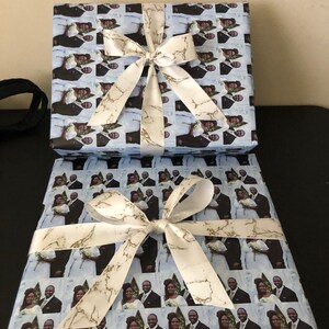 Op de afbeelding: Twee cadeaudozen verpakt in blauw en wit gepatroneerd papier met een wit satijnen lint met gouden marmeraccenten. Het patroon op het papier is een herhaald beeld van een stel.