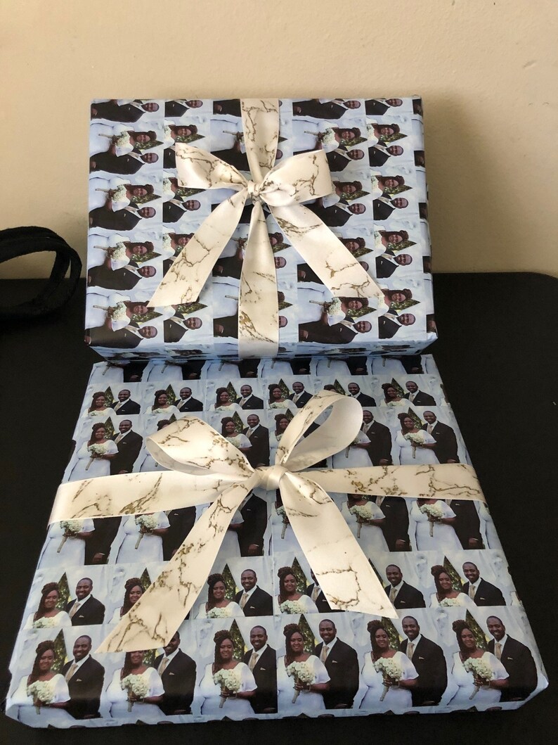 Op de afbeelding: Twee cadeaudozen verpakt in blauw en wit gepatroneerd papier met een wit satijnen lint met gouden marmeraccenten. Het patroon op het papier is een herhaald beeld van een stel.