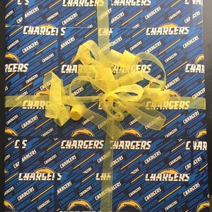 Op de afbeelding: Een blauwe en gele cadeauverpakking met een herhalend patroon van het logo van de Los Angeles Chargers. Het cadeau is ingepakt met een geel lint en strik.