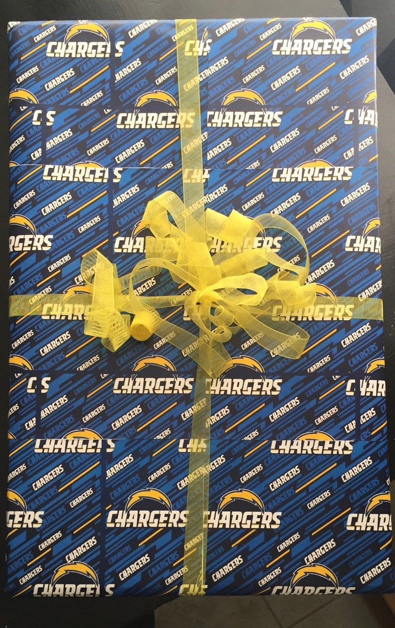 Op de afbeelding: Een blauwe en gele cadeauverpakking met een herhalend patroon van het logo van de Los Angeles Chargers. Het cadeau is ingepakt met een geel lint en strik.