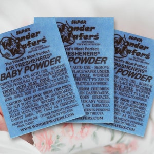 Może przedstawiać: Trzy niebieskie saszetki odświeżacza powietrza z nadrukiem "Super Wonder Wafers" i "The World's Most Perfect Air Fresheners Baby Powder". Saszetki są wykonane z cienkiego, niebieskiego materiału i mają białą obwódkę. Tekst jest czarny.
