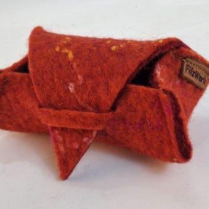 May include: A handmade, red felt pouch with a unique folded design. The felt has a textured appearance with small, colorful flecks. A small, brown leather tag with the text "FilzWerk" is attached.