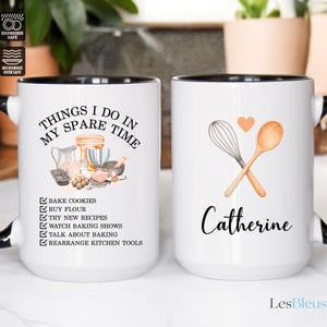 May include: White ceramic mug with a black handle and rim. The mug features the text "THINGS I DO IN MY SPARE TIME" and a list of baking-related activities. The other mug has a whisk and spoon graphic with the name "Catherine".