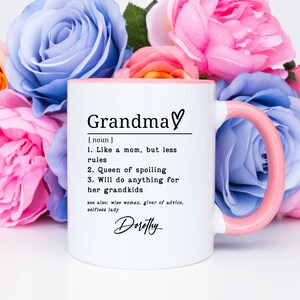 Pu&ograve; includere: Tazza in ceramica bianca con interno e manico rosa, con la definizione di "Nonna" in testo nero. La definizione include frasi come "Regina dello viziare" e "Far&agrave; di tutto per i suoi nipoti". La tazza &egrave; circondata da fiori rosa e blu.