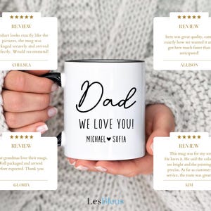 May include: White ceramic mug with black handle and rim, featuring the words "Dad WE LOVE YOU!" in black script, along with the names "Michael & Sofia." The mug is held by a person.
