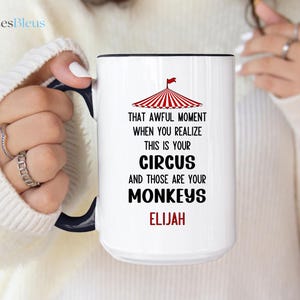May include: White ceramic mug with a black handle and rim. The mug features a circus tent graphic and the text "THAT AWFUL MOMENT WHEN YOU REALIZE THIS IS YOUR CIRCUS AND THOSE ARE YOUR MONKEYS ELIJAH."