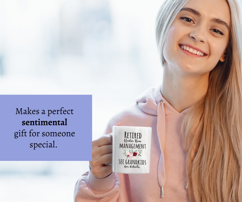 May include: White ceramic mug with black text that reads "RETIRED Under New MANAGEMENT SEE GRANDKIDS for details". The mug has a floral design with pink, red, and green flowers.