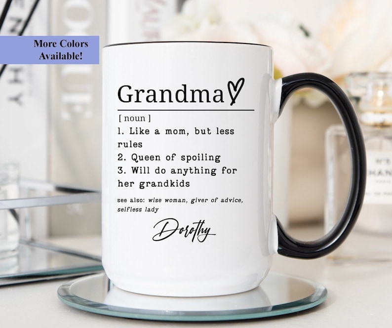 Pu&ograve; includere: Tazza in ceramica bianca con manico e bordo neri. La tazza presenta la definizione di "Nonna" con un simbolo a cuore e il nome "Dorothy" in corsivo. La tazza &egrave; appoggiata su un sottobicchiere di vetro trasparente.