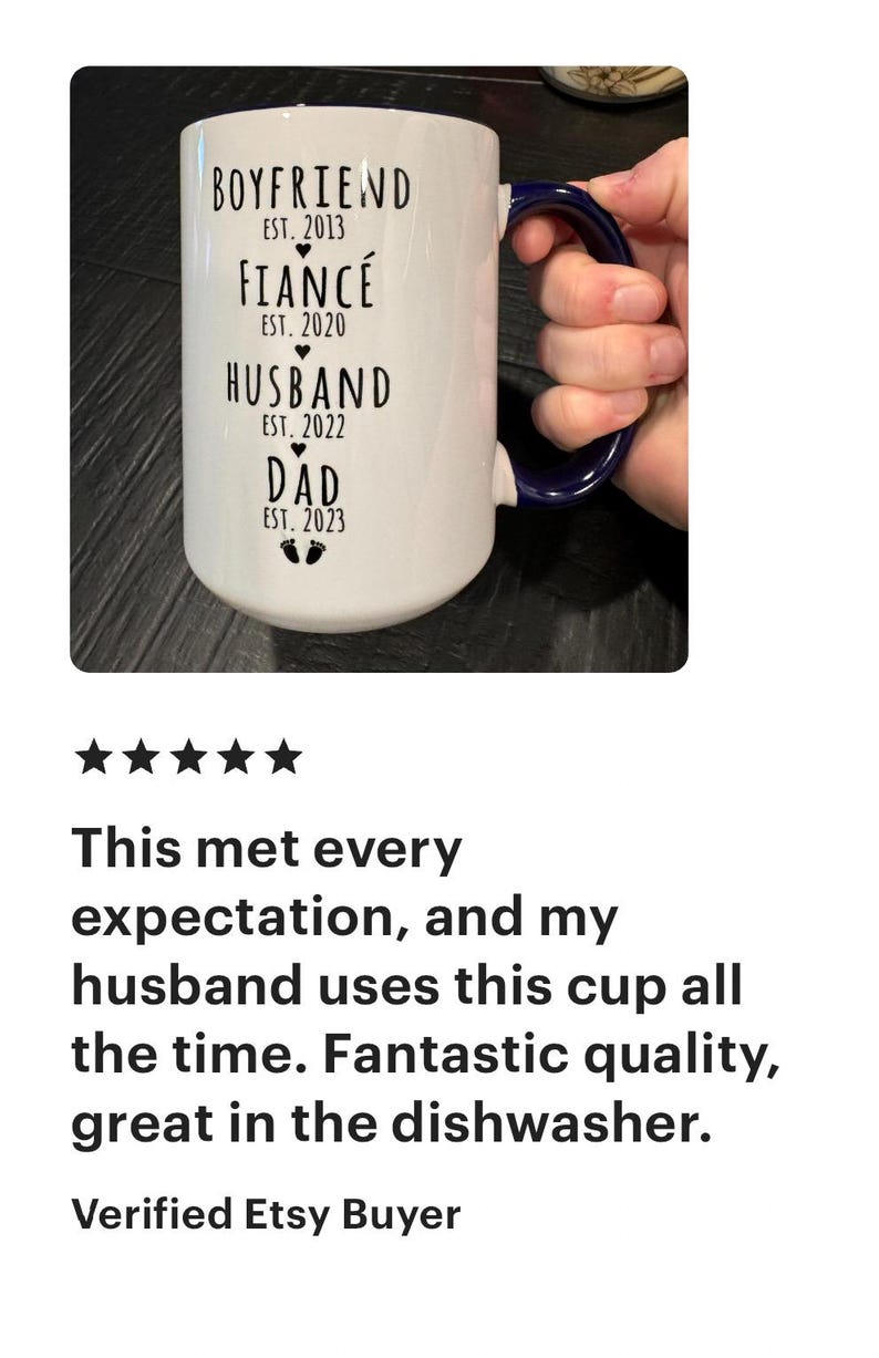 May include: White ceramic mug with a blue handle. The mug has black text that reads "Boyfriend Est. 2013, Fianc&eacute; Est. 2020, Husband Est. 2022, Dad Est. 2023".