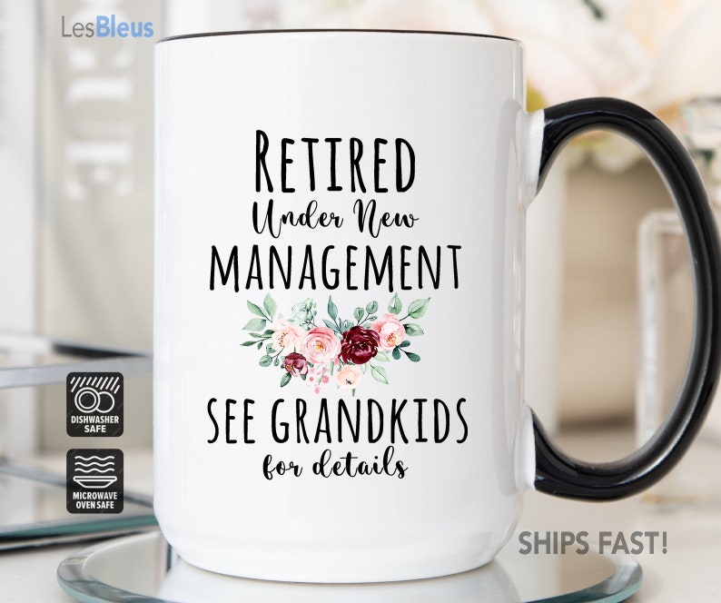 May include: White ceramic coffee mug with a black handle. The mug has a floral design and the text "RETIRED Under New MANAGEMENT SEE GRANDKIDS for details". The mug is dishwasher and microwave safe.