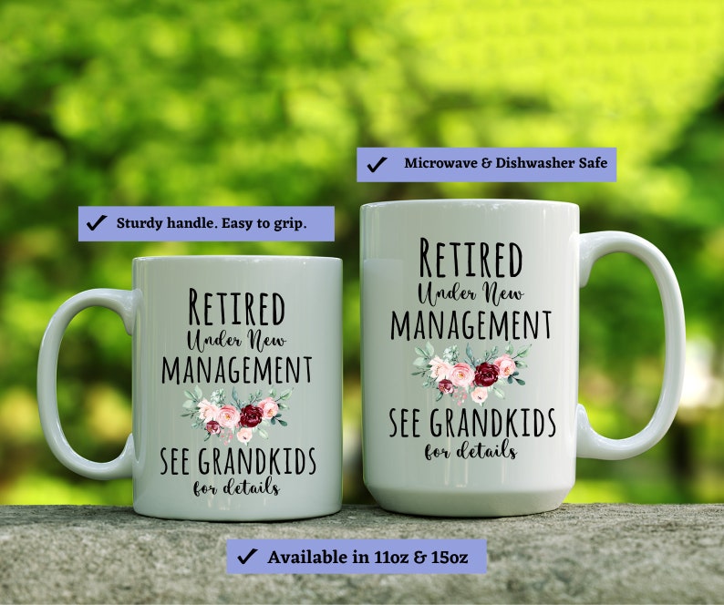 May include: Two white ceramic mugs with black text that reads "Retired Under New Management See Grandkids for details". The mugs have a floral design with pink, red, and white flowers. The text is on a white background. The mugs are microwave and dishwasher safe.