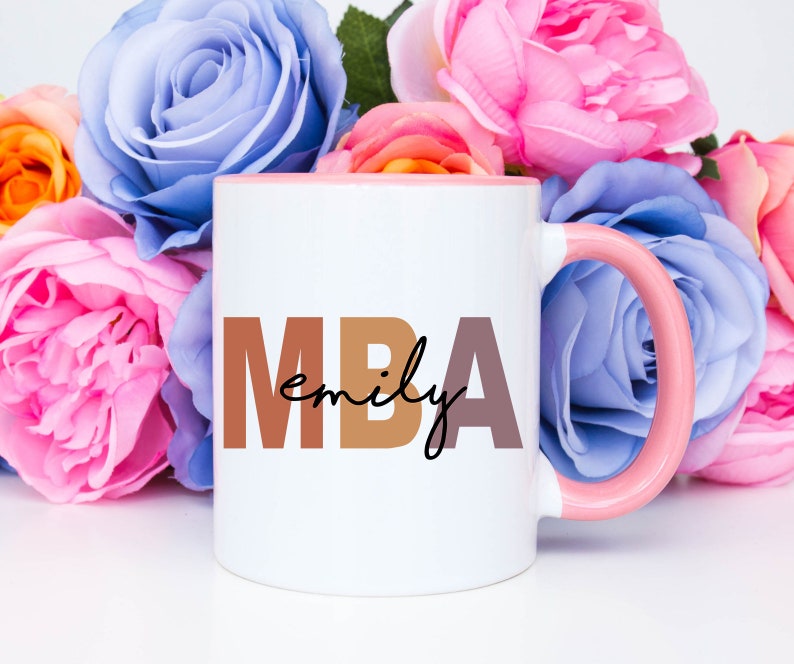 Może przedstawiać: Biały kubek ceramiczny z r&oacute;żowym rantem i uchwytem. Kubek ma nadrukowany tekst "MBA emily" brązowymi i r&oacute;żowymi literami.
