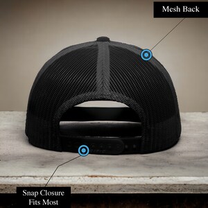 K&ouml;nnte beinhalten: Schwarze Baseballkappe mit Mesh-R&uuml;cken und Druckknopfverschluss. Die Kappe hat ein schwarzes Schild und einen schwarzen Mesh-R&uuml;cken.