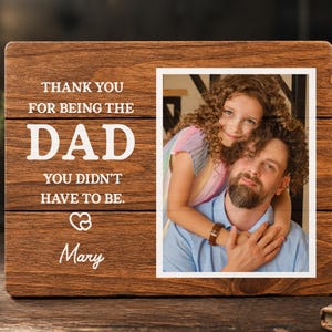 May include: A wooden picture frame with a photo of a man and a girl. The frame has the text "THANK YOU FOR BEING THE DAD YOU DIDN'T HAVE TO BE." and the name "Mary" in white lettering.