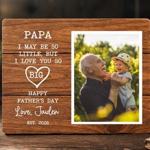 May include: Wooden photo frame with a picture of a man and a child. The frame has the words "PAPA, I MAY BE SO LITTLE, BUT I LOVE YOU SO BIG, HAPPY FATHER'S DAY, Love, Jaiden, EST. 2026" in white lettering.